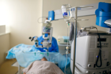 Physiological solution in the form of a dropper close-up in the ward of the hospital. Doctor and patient who lies on a bed in a ward room