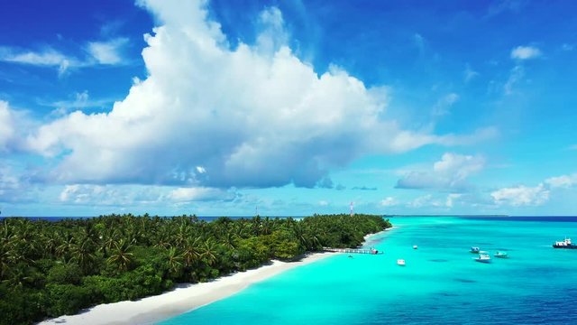 aerial drone parallax shot of tropical uninhabited island with cocos palms surrounded by crystal clear ocean water