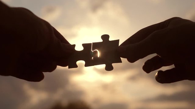 teamwork business finance concept. male hands connect two puzzles silhouette against the sunset. symbol teamwork of association and connection. strategy lifestyle business