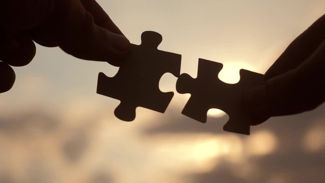 teamwork business finance concept. male hands connect two puzzles against silhouette the sunset. lifestyle symbol teamwork of association and connection. strategy business