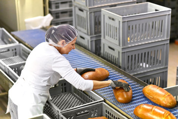 Frau arbeitet am Fliessband mit Broten in der Lebensmittelindustrie - Großbäckerei // Woman works...