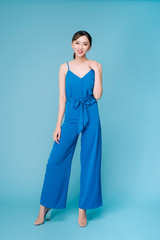 Young beautiful woman posing in new casual blue fashion costume dress with pants full body on blue background