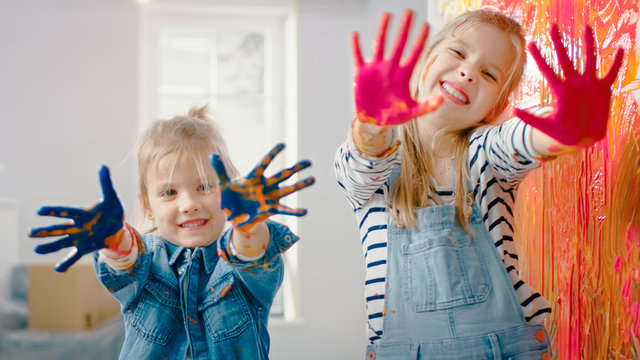 Two Fun Little Sisters Show Their Hands that are Dipped in Colorful Paint. They are Happy and Laugh. Sisterhood Goals. Redecoration at Home.