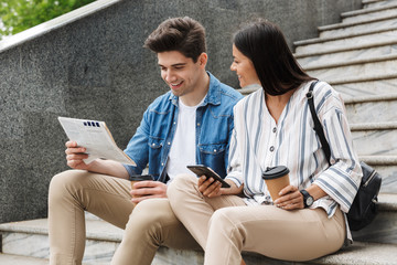 Happy young amazing loving couple business people colleagues outdoors outside on steps reading...