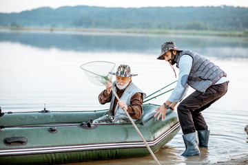 Grandfather with son preparing for the fishing, pushing out the boat on the lake early in the...