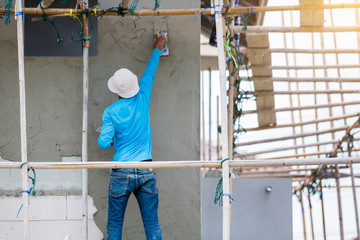 plasterer in blue working uniform plastering the wall of house building site. hands plasterer...