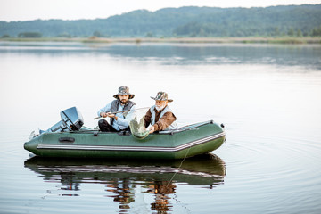 Grandfather with adult son fishing on the inflatable boat on the lake early in the morning