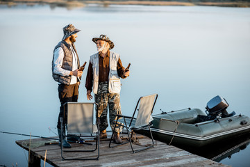 Obraz premium Grandfather with adult son having warm conversation while fishing together on the pier near the lake early in the morning