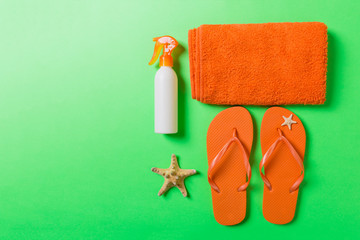 Top view of Beach flat lay accessories. sunscreen bottle with seashells, starfish, towel and flip-flop on Colored background with copy space