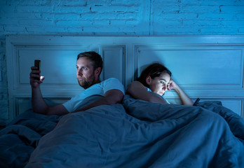 Fototapeta na wymiar Sad and bored couple addicted to smart mobile phones late at night in phase of mutual disinterest