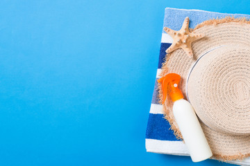 Summer beach flat lay accessories. Sunscreen bottle cream, straw hat, towel and seashells on colored Background. Travel holiday concept with copy space