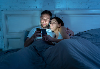 Fototapeta na wymiar Couple on mobile phones in bed late at night enjoying social network, games and internet connection