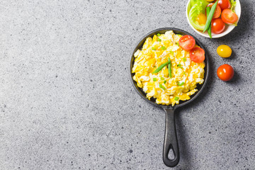 Scrambled eggs in cast iron skillet with cherry tomatoes . Top view, space for text.