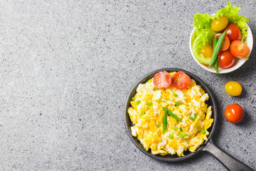 Scrambled eggs in cast iron skillet with cherry tomatoes . Top view, space for text.