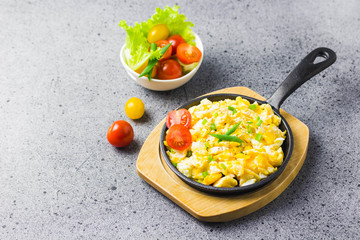 Soft creamy scrambled eggs in cast iron skillet and cherry tomatoes. Selective focus, space for text.