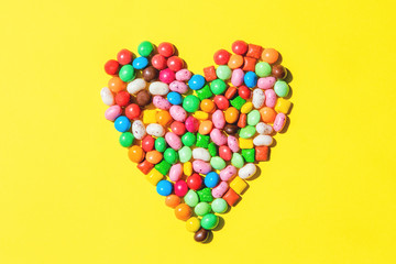Heart shape made of small colorfull candies on bright yellow background. Sweets for birthday concept. Valentine's day design. Top view, flat lay.