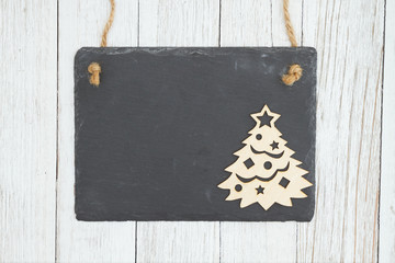 Blank hanging chalkboard with a Christmas tree on weathered whitewash textured wood background