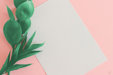 White sheet of paper with green tropical leaves on a pink background top view mockup. Floral background for lettering with copy space in pastel colors