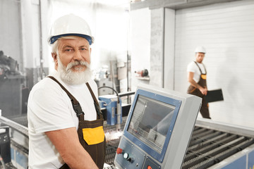 Wlder male worker of metal factory standing near computer