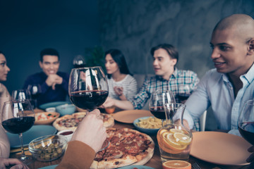 Cropped close up photo communicating company social crowd event hang out best members different race guys raise glasses beverage sit table shirts formal-wear sweater pullover loft room indoors