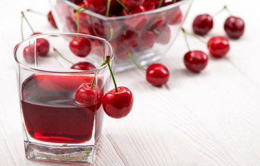 A lot of red, ripe cherries with a glass of cherry juice on a white background