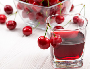 A lot of red, ripe cherries with a glass of cherry juice on a white background