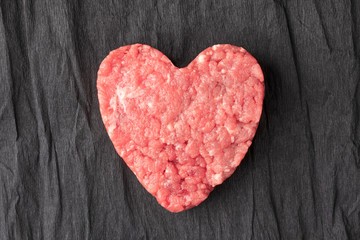 Uncooked ground beef patty on a background of crumpled black paper