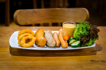 Mix grilled sausages with onion ring and salad set is served on wooden table. Selected focus food photo.