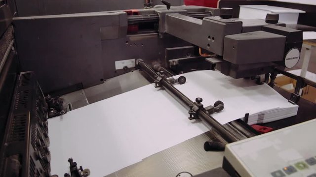 Printed sheet of paper coming out from printing machine. Offset printing, CMYK, close up