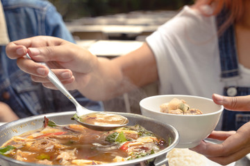 Woman serving steaming hot Asian soup into a bowl at a restaurant during a family meal - Young female diner at a table holding spoon full of Thai Tom Yum spicy soup with summer filter