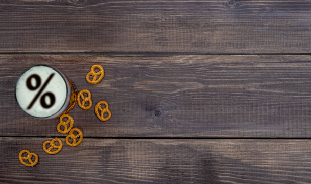 Beer with percent sign on a beer foam and pretzels on dark wooden background. Top view. Empty space for text