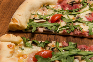 closeup two halves of pizza with arugula, ham, mushrooms and tomatoes
