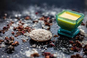 Face mask for skin whitening on wooden surface consisting of besan or gram flour and some rose water. With some dried rose petals and gram flour spread on the surface. Horizontal shot.
