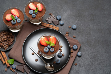 Classic tiramisu dessert with blueberries and strawberries in a glass on stone serving board on dark concrete background