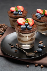 Classic tiramisu dessert with blueberries and strawberries in a glass on stone serving board on dark concrete background