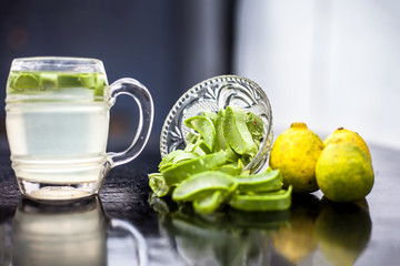 Close up of glass mug on wooden surface containing aloe vera and lemon juice detox drink along with its entire raw ingredients with it. Horizontal shot with blurred background.
