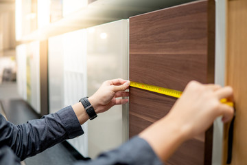 Male hand using tape measure on cabinet panel choosing materials or countertops for built-in...