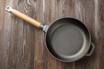 Cast iron pan on rustic wooden  background, top view.