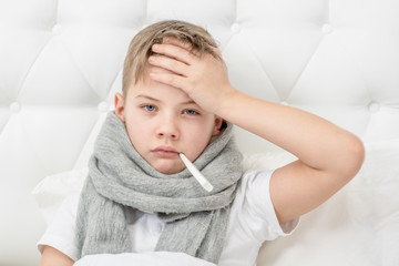 Sad sick young boy with thermometer in his mouth at home