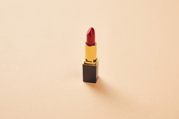 single opened tube of red lipstick on beige