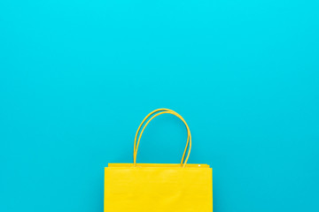 shopping paper bag on the turquoise blue background. flat lay photo of yellow bag. summer sale concept with copy space.