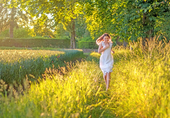 Fototapeta premium Beautiful preteen barefoot girl running through high grass in the fields at warm sunny day. Golden sunset. Summer lifestyle and leisure activity