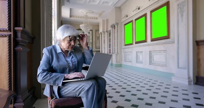 Aged woman working on laptop in art gallery