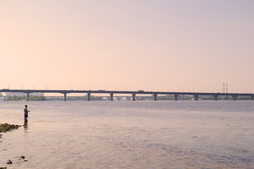 Man fishing in the river near the bridge.