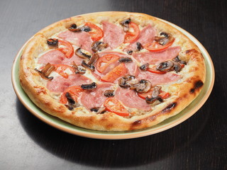 Pizza with ham, tomatoes and mushrooms in a plate
