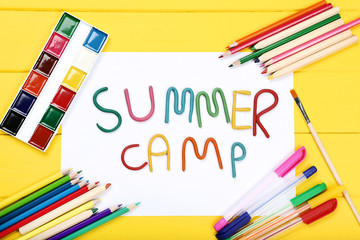 Text Summer camp with school supplies on yellow wooden table