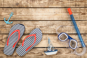 Pair of flip flops with diving mask and decorative ship on brown wooden table