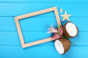 Fototapeta na wymiar Wooden blank frame with seashells and coconuts on blue table