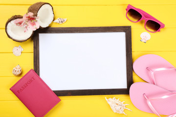 Wooden blank frame with seashells, clothing and coconuts on yellow table