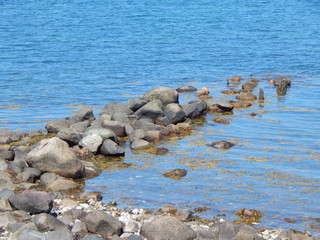 Verfallener Wellenbrecher aus Steinen an der Küste, blaues Wasser und Algen